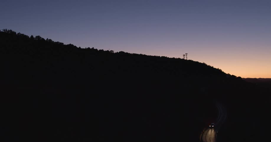 A vehicle drives down the dark road on the hill below