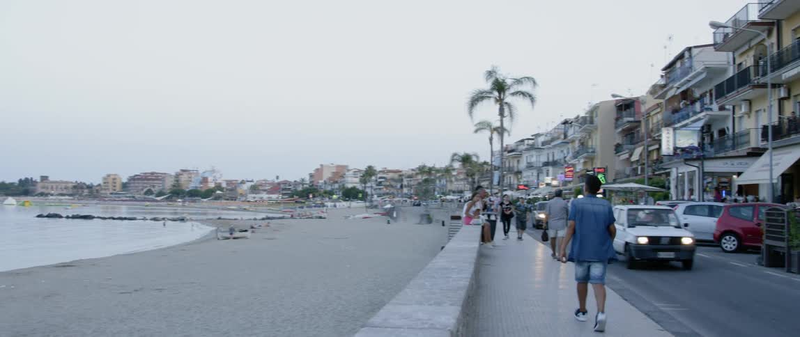 People walk along a street by the water