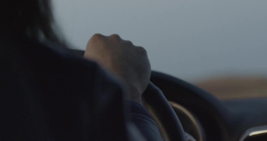 Person holds steering wheel and drives the car at dusk