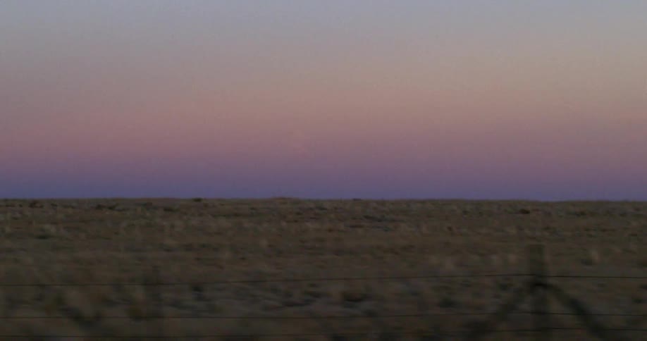 Passing by fenced in fields of grass at sunset