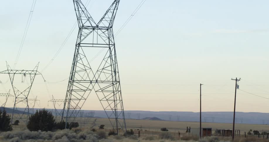 Large power line towers cross countryside toward mountains
