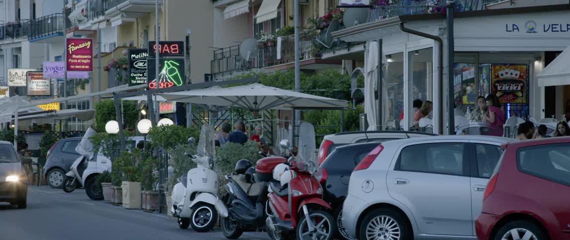 Motorbikes and cars line a city sidewalk in the afternoon