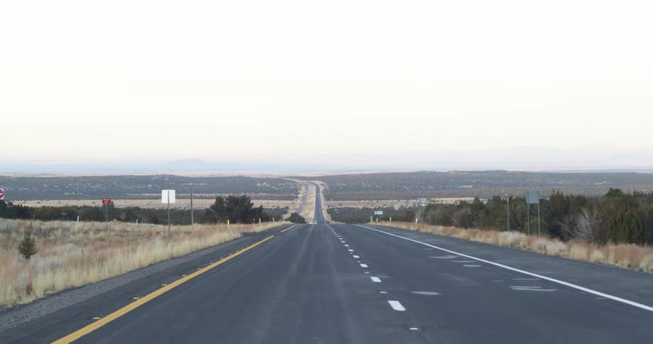 An empty rural highway with a dotted white line goes all the way to the horizon
