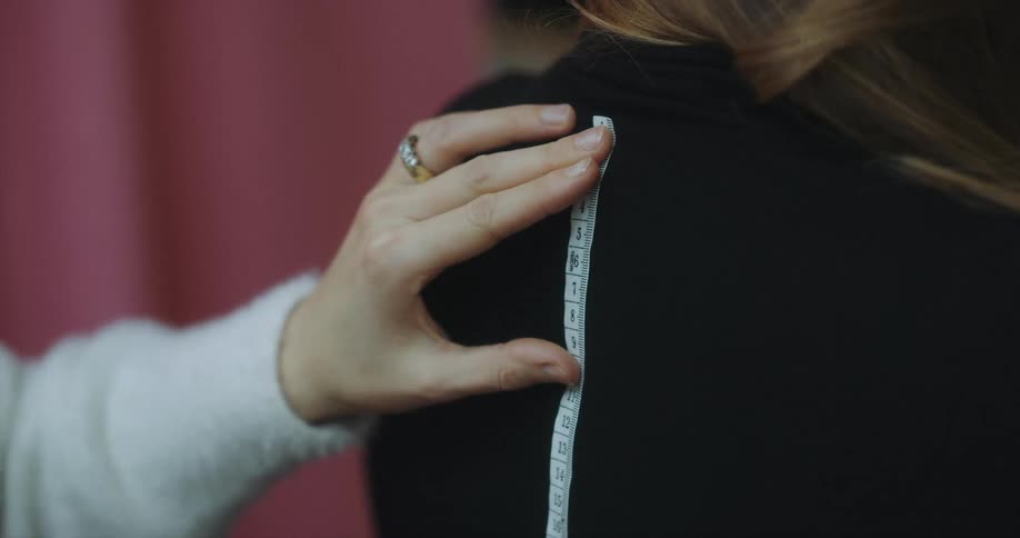 A person with a ring using a measuring tape to measure a womans back