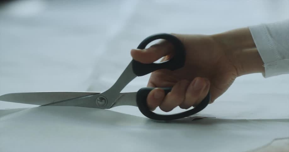 A woman uses fabric scissors to cut a large piece of paper held together with sewing needles