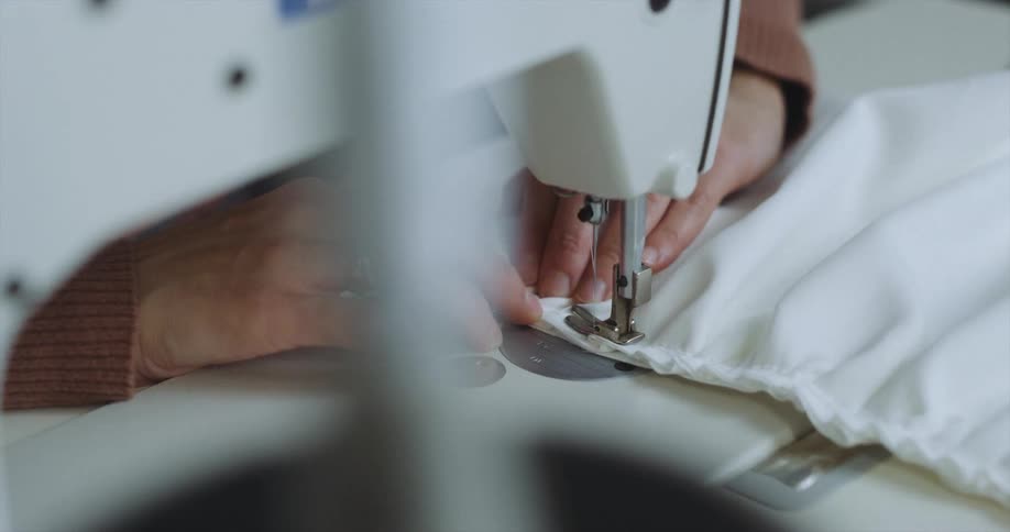 Person sews seam of white fabric on white sewing machine