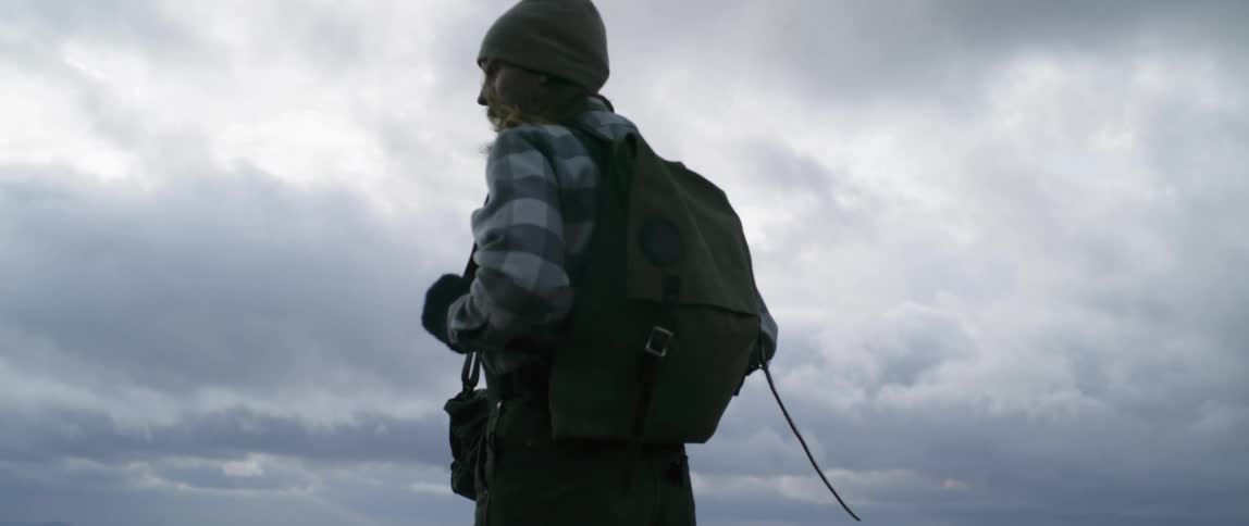 Man wearing backpack is standing outside on windy and cloudy day