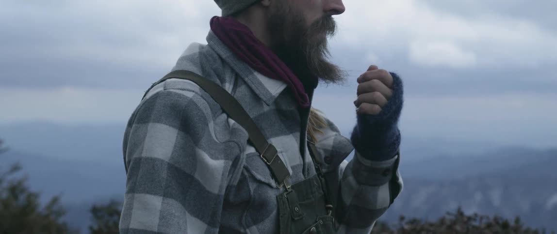 Man strokes his beard as he stands under a cloudy sky