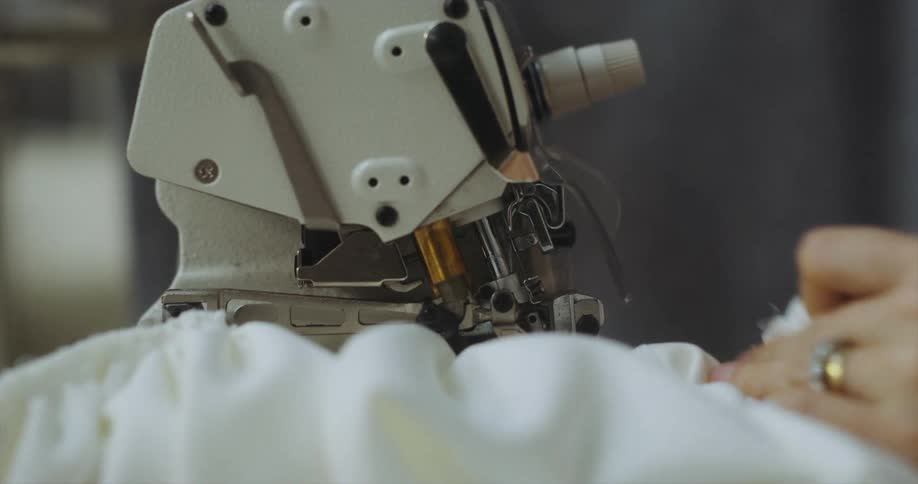 A woman sews a large piece of white fabric