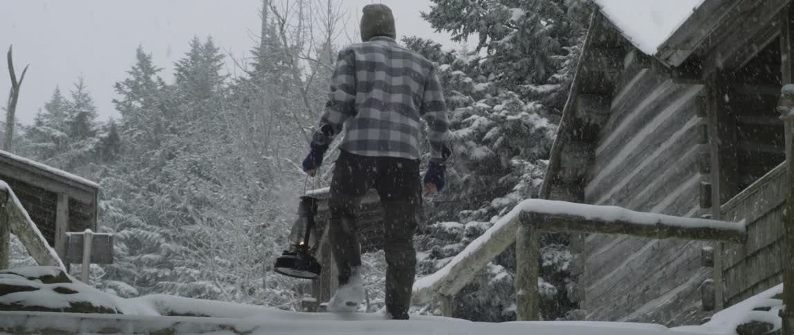 Man is carrying lantern up stairs to cabin in snow storm