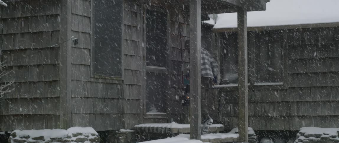 Snow falls gently as a man walks up the steps and opens a door