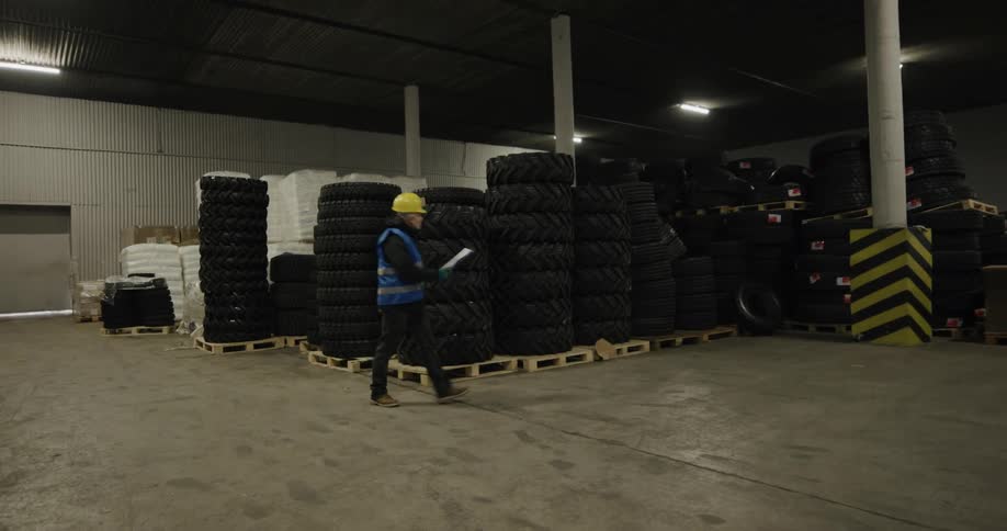 A man in a hard hat walks through a warehouse filled with stacks of tires