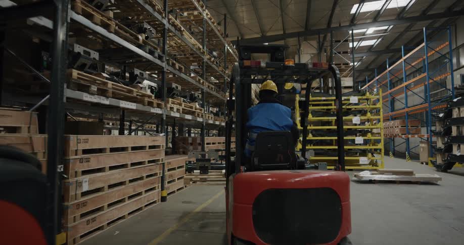 Man drives loader carrying inventory down aisle in warehouse
