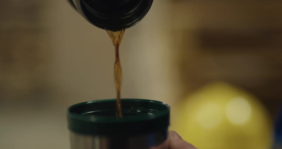 A man pours coffee out of a thermos into the cap cup and raises his hand to drink