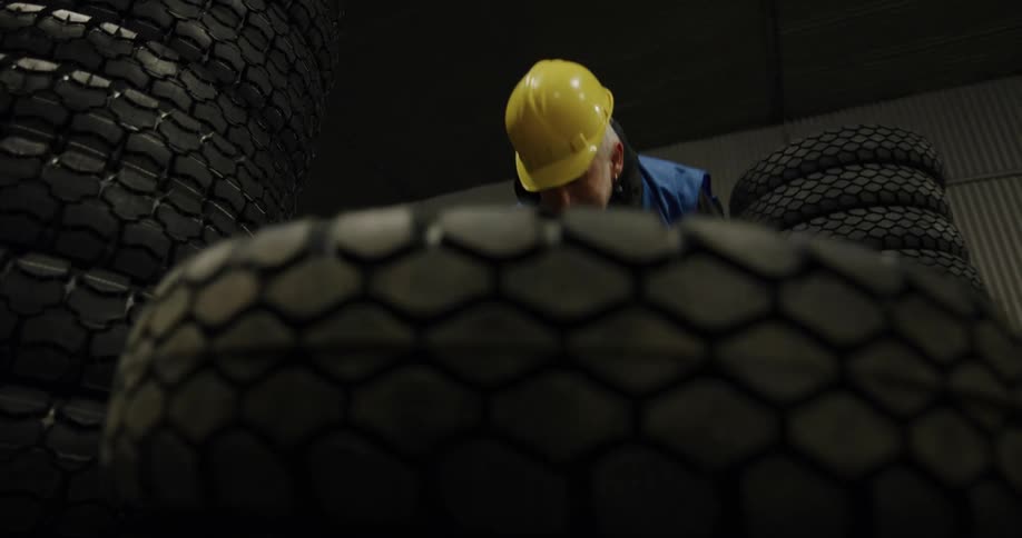 A man rolls a tire through a room before placing it atop a stack of tires