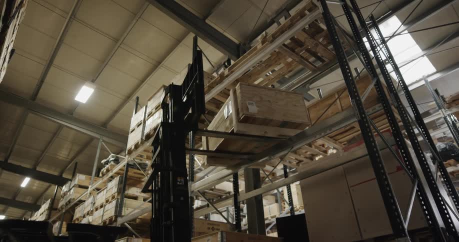 Warehouse worker uses a forklift to place a wooden crate on the shelf of a tall aisle