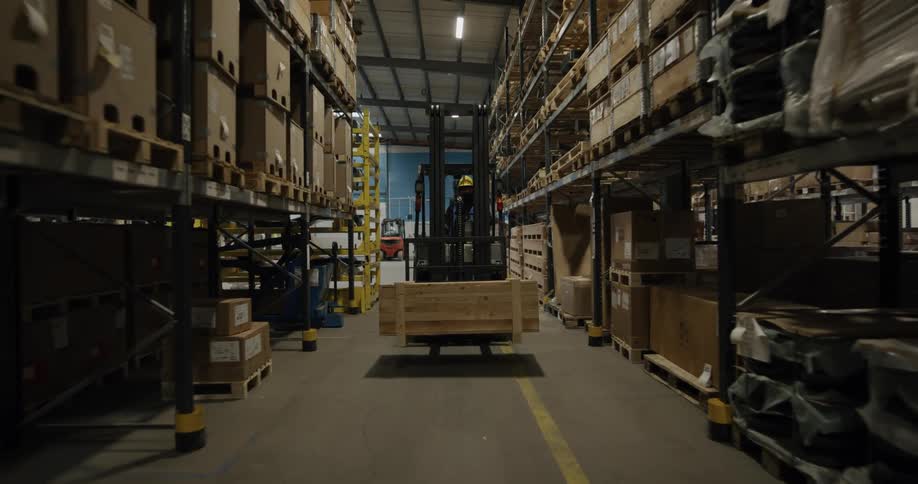 A man with a vest and hardhat operating a forklift in a warehouse