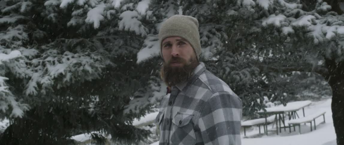 Man is standing outside and staring off as it snows