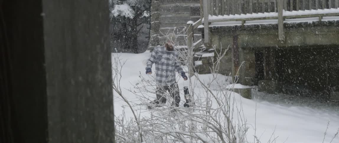 Man exits a log cabin during a snowstorm