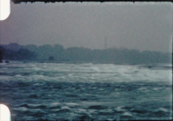 Waves flow under bridge and against forest covered shore on foggy day
