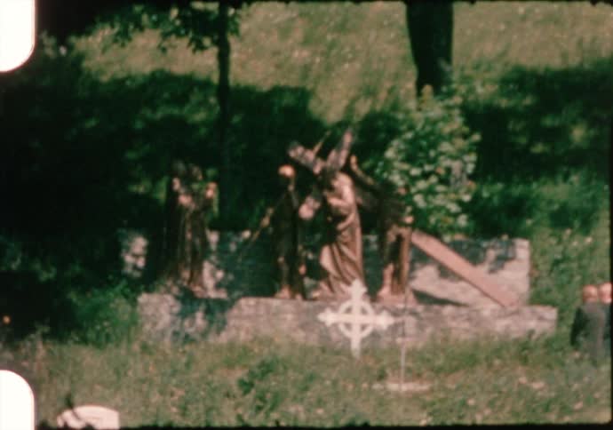 People walk through graveyard past statues on sunny day
