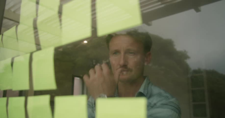 A man places yellow sticky notes on a glass window and stops to look at them