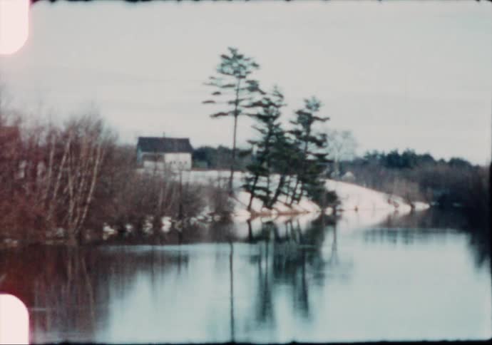 A lake in a rural area with snow on the shore and a house just off it