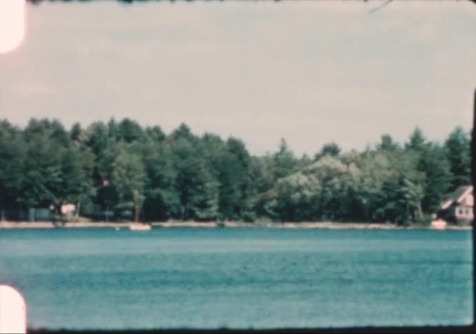 A small boats sails in a lake near lakefront homes that are surrounded by woods