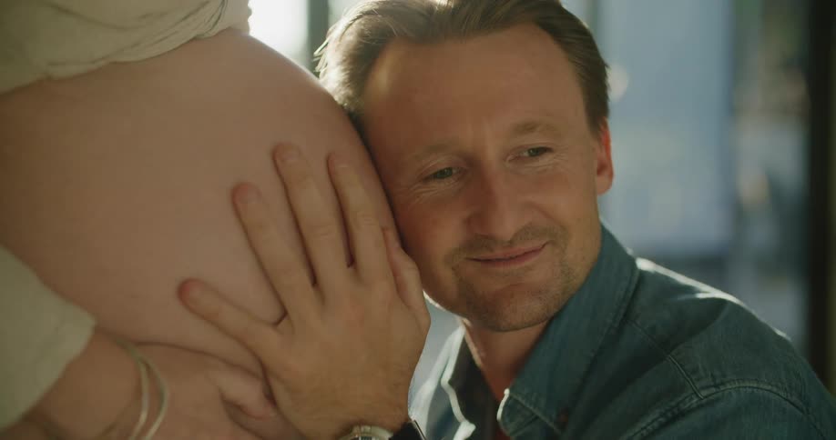 A man leans his ear against his wifes pregnant belly