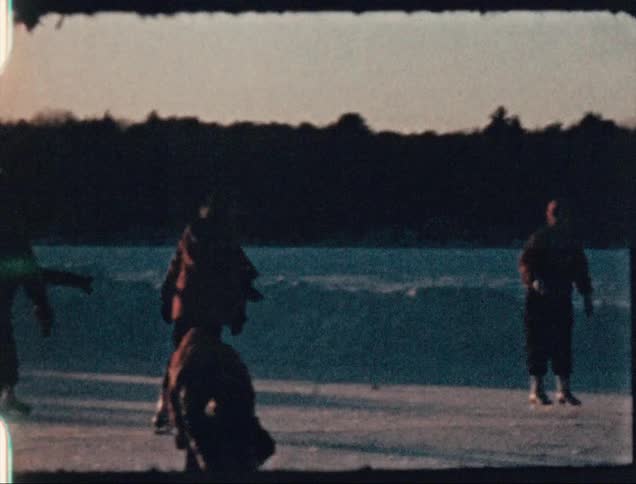 A group of people ice skate atop a frozen lake during the day