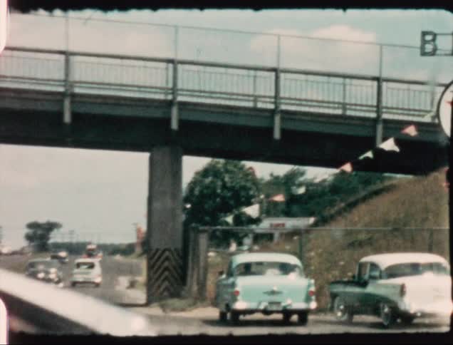 Classic cars drive under an overpass on the freeway near a neighborhood