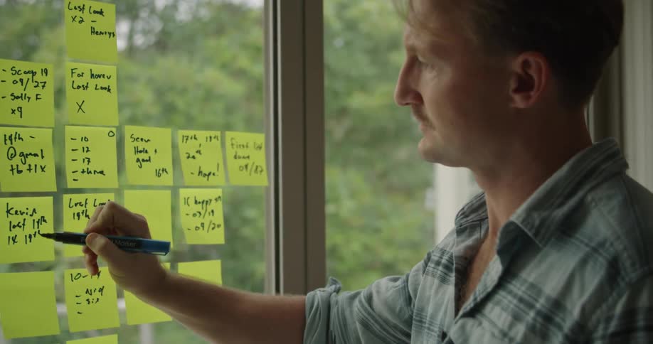 A man writes on sticky notes hanging on a window