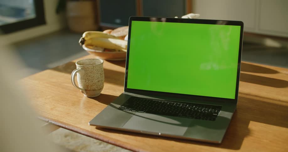 Person points at a laptop next to a coffee cup on a table in the kitchen