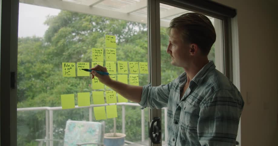 A man writes on sticky notes on his patio window