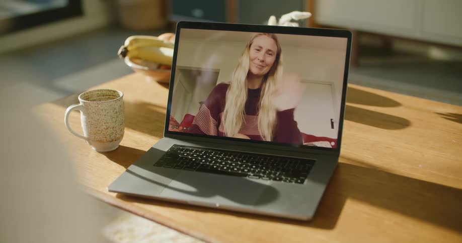 A person in a room video chatting on a laptop on a table next to a mug with a hot drink