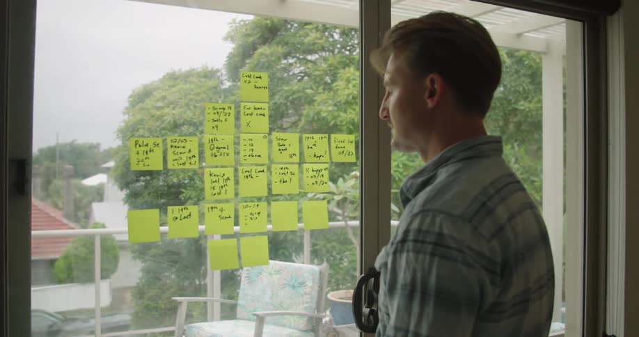 Man makes noteson post it notes stuck on sliding glass door as traffic passes through neighborhood