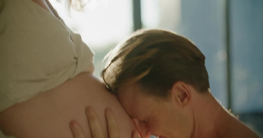 Father kneels touching forehead to pregnant abdomen of mother