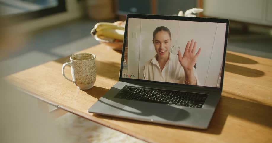 A woman on a video call on a laptop waves goodbye