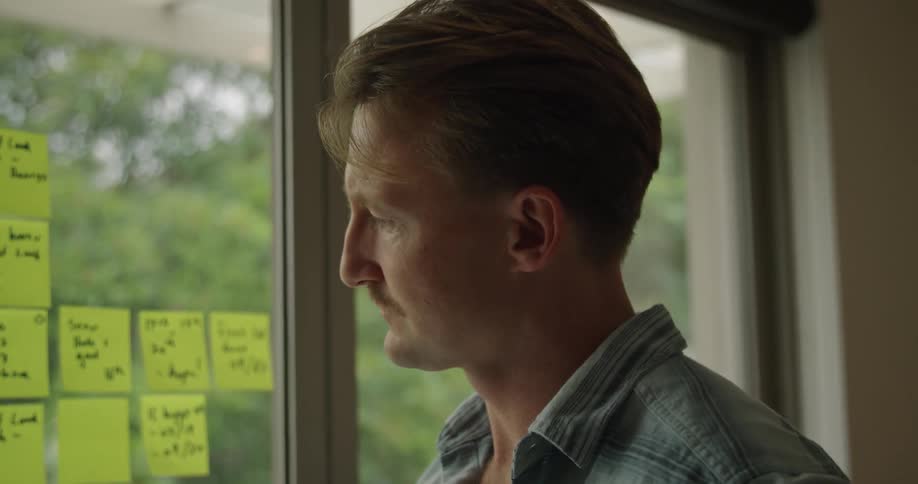 A man working from home writes out ideas on yellow sticky notes arranged on his sliding glass door