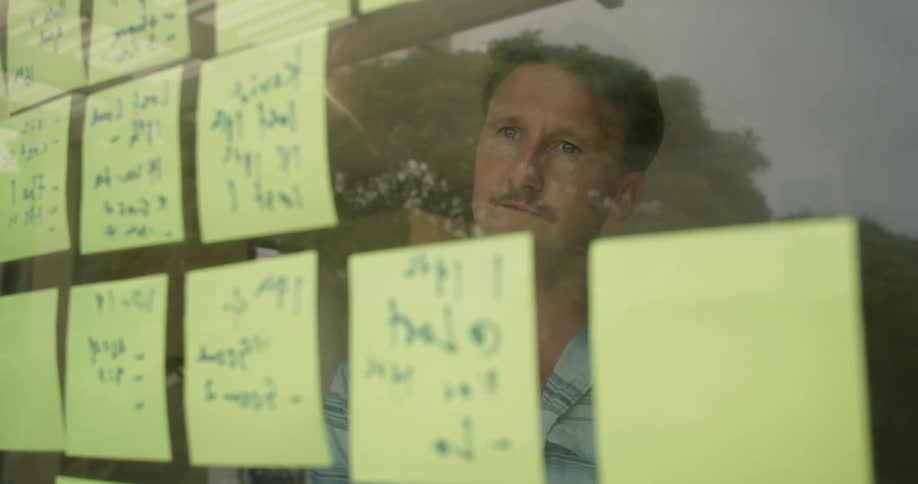 Man working in the office at home writing on post its taped in a glass door