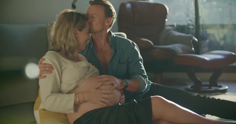 Parents to be cuddle on floor in living room stroking pregnant abdomen