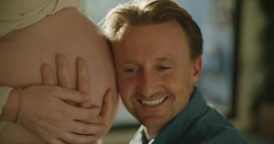 A view of a man listening to a pregnant womans belly