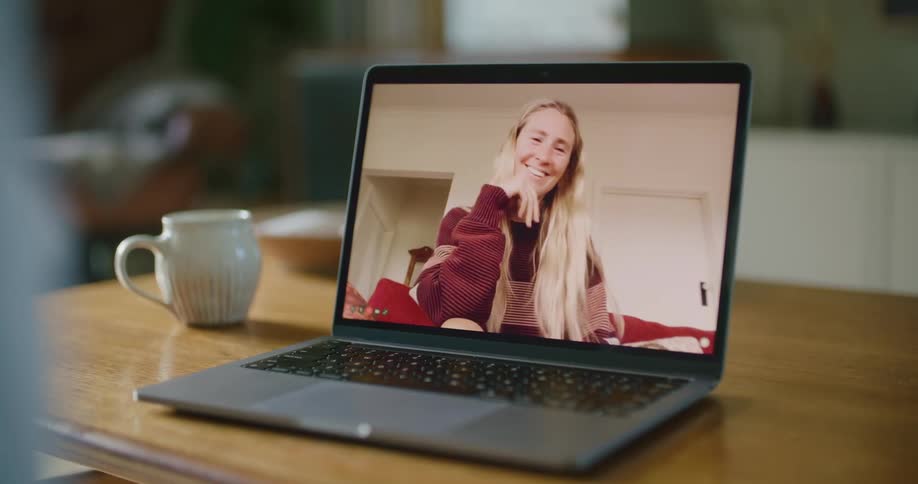 A laptop in a room on a table next to a mug with a hot smoking drink