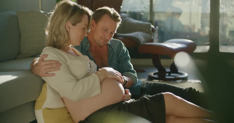 Couple cuddle sitting on floor near balcony touching womans pregnant belly