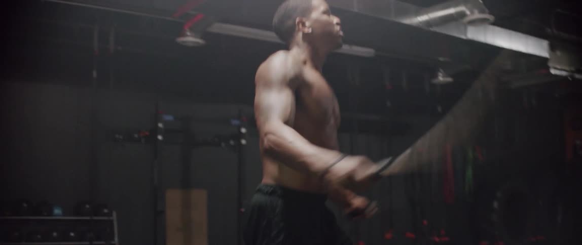 Shirtless man quickly jumps rope in a gym