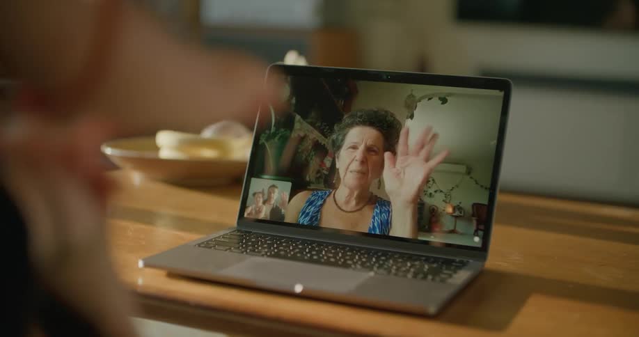 A woman is on a video call seen on a laptop and waves goodbye