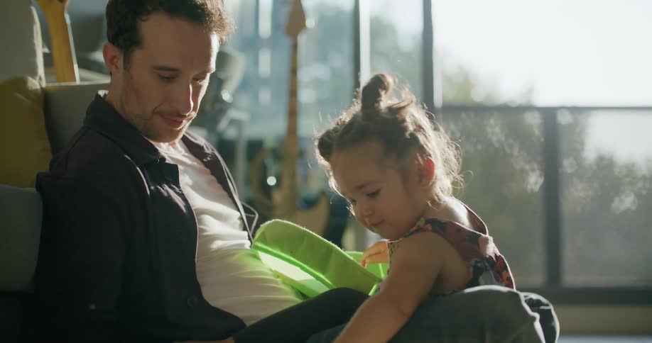 Father sits on floor with daughter as she draws
