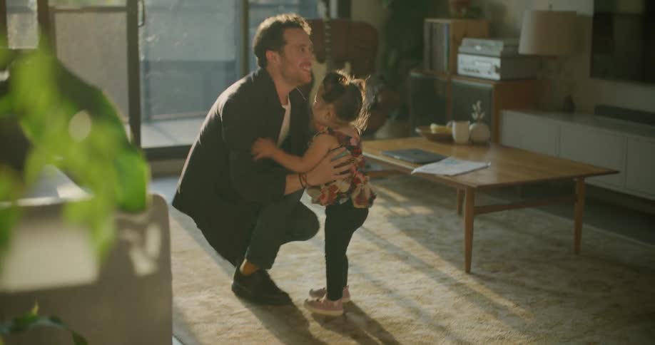 Father lifts up his little daugther on the livingroom at sunset