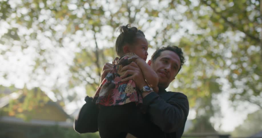 A dad hugging his young daughter picks her up while standing near a parking lot