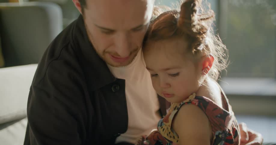 A man holds a small girl in his lap as he draws a picture on a piece of paper with a marker